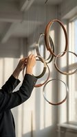 Person arranging modern circular metal rings hanging art installation in minimalist interior with natural sunlight shadows creating contemporary home decor.