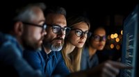 Diverse team of professionals analyzing data on computer screens in dark office environment. Collaborative work session with focused concentration and teamwork.