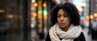 Young African American woman with curly hair wearing beige scarf in urban evening setting with bokeh lights for lifestyle and portrait concepts.