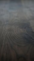 Close-up of dark wood grain texture showing natural growth rings and annual rings pattern. Shallow depth of field emphasizes wood surface details for design and background use.