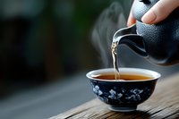 Hot tea pouring from teapot into traditional ceramic bowl with floral design on wooden surface, beverage preparation.