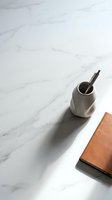 Minimalist workspace with ceramic pen holder and leather notebook on white marble surface for modern office design and productivity concepts.