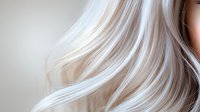 Flowing platinum blonde hair strands in gentle motion against soft beige background, creating elegant waves and highlighting natural shine and texture.