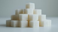 White sugar cubes stacked in pyramid formation against light background, showing crystalline texture and geometric shapes in minimalist composition for food industry concept.