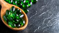 Green translucent vitamin supplements in wooden spoon on dark stone background, macro shot with selective focus. Natural health concept for wellness products.