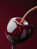 Fresh ripe dark cherry with stem covered in liquid chocolate against burgundy background, macro shot showing glossy texture and reflection.