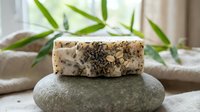 Natural exfoliating soap bar with organic ingredients and crushed seeds on smooth stone, spa wellness product for skincare routine.