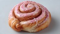 Freshly baked cinnamon roll pastry with pink icing glaze and sugar crystals on white background, isolated sweet bakery dessert for breakfast menu design.