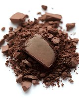 Rich cocoa powder scattered with dark chocolate pieces and chunks on white background, isolated for baking and confectionery design projects.