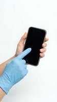 Hand wearing blue latex glove holding smartphone with blank black screen against white background, suitable for healthcare, medical, technology, and safety applications.