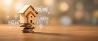 Wooden house model on coins with rising percentage arrows showing real estate investment growth and property value appreciation on warm bokeh background.