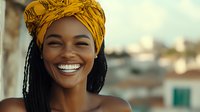 Young African woman with bright smile wearing yellow headwrap and natural dreadlocks hairstyle against blurred urban background, radiating joy and confidence.