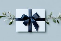 White gift box with elegant navy blue satin ribbon bow and eucalyptus branches on light gray background, styled for special occasions and celebrations.