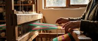 Skilled artisan weaving colorful threads on traditional wooden loom in sunlit workshop, creating handmade textile with intricate patterns and vibrant colors.