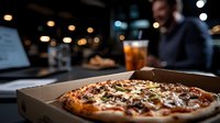 Fresh baked pizza with mushrooms and cheese in cardboard box at restaurant with blurred background of dining atmosphere and warm lighting for food delivery.