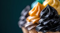 Colorful swirled frosting peaks in black, orange, yellow and white against dark background, macro food photography showing texture and detail for bakery and dessert designs.
