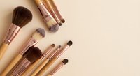 Professional makeup brushes with rose gold ferrules arranged on neutral beige background for beauty and cosmetics applications.