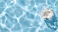 Underwater pool drain with sunlight creating ripple patterns on blue water surface, white metal drain cover visible through crystal clear swimming pool water.