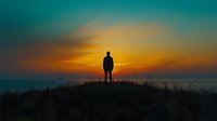 Silhouette of person standing alone on hilltop against dramatic orange and teal sunset sky, with tall grass in foreground creating moody atmospheric scene.