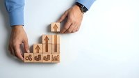 Business professional arranging wooden blocks with growth arrows and success icons representing career development and strategic planning concepts.