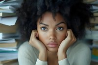 Young African American woman student feeling overwhelmed surrounded by stacks of books studying academic stress burnout education pressure concept.