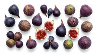 Fresh figs arranged on white background, whole and halved fruits showing red interior flesh and seeds, overhead flat lay composition for food styling and culinary use.