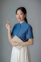 Young Asian woman in blue shirt and white skirt holding laptop while pointing upward with idea gesture against neutral gray background.