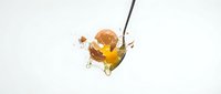 Wooden spoon dripping golden honey with dynamic splash and droplets against clean white background for culinary and food photography projects.