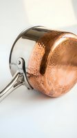 Copper and stainless steel saucepan with hammered texture and steel handle on white background for culinary cooking kitchen equipment design.