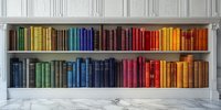 Colorful vintage books arranged by spectrum colors on built-in white shelves against classic wall paneling, creating rainbow library effect on marble floor.
