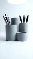 Modern gray concrete pen holders with black pens and pencils on white desk. Minimalist office organization and workspace storage solution.