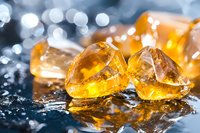 Golden amber gemstones with water droplets on reflective surface creating bokeh light effects for jewelry and luxury product design.