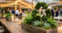 Rustic wooden box filled with green succulents and ferns creates natural centerpiece for outdoor wedding reception with string lights and guests dining.
