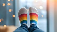 Cozy rainbow striped socks on feet against blurred bokeh lights background, representing comfort, diversity and relaxation at home during winter season.