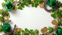 St. Patrick's Day themed flat lay with green leprechaun hats, horseshoes, gold coins and clover leaves arranged on white background with copy space.