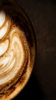 Overhead view of cappuccino with latte art foam design in ceramic cup on dark background, suitable for coffee shop menus and beverage marketing.