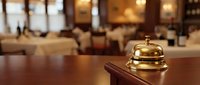 Golden brass service bell on wooden hotel reception desk with blurred luxury lobby background. Hospitality industry concept for guest services and accommodation.