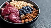 Fresh bowl with raw tuna, blueberries, almonds and chickpeas on dark background. Healthy protein-rich ingredients for balanced nutrition and meal prep.