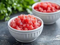 Fresh diced watermelon cubes in white ceramic bowls on dark stone background with green herbs, ready for healthy summer snack or fruit salad preparation.