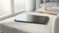 Modern tablet computer lying flat on beige fabric sofa in bright living room with natural window light for digital lifestyle and home technology concepts.