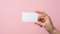 Close-up of a hand holding a blank white card against a soft pink background, suitable for business card mockups, branding presentations, and marketing materials.