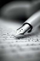 Close-up macro shot of fountain pen nib writing on paper with handwritten text in black and white, shallow depth of field creates artistic blur effect.
