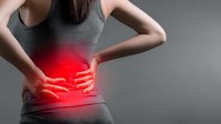 Woman in gray tank top with hands on lower back, red glow highlighting pain area against neutral background, illustrating back pain or injury.