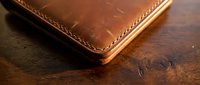 Handcrafted brown leather wallet with detailed stitching on rustic wooden surface showcasing traditional craftsmanship and quality materials.