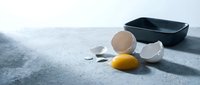 Broken egg with yolk and shell fragments scattered on kitchen counter near dark bowl, cooking accident and food preparation mishap concept.
