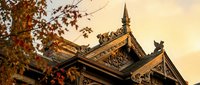 Traditional Asian temple roof with ornate wooden carvings and decorative elements against warm sunset sky, showcasing classical architecture details.
