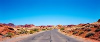 Straight asphalt road stretching through red desert landscape with sparse vegetation under clear blue sky, suitable for travel and adventure concepts.