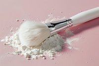 White makeup brush with scattered loose face powder on pink background, creating dynamic cosmetic composition for beauty and makeup artistry concepts.
