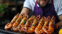 Grilled jumbo shrimp with herbs and lemon on black stone plate, served by bearded chef in purple apron. Fresh seafood with charred marks and garnish.