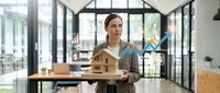 Young male architect of mixed ethnicity presenting wooden architectural model with upward growth chart overlay in modern office space with large windows and contemporary furnishings.